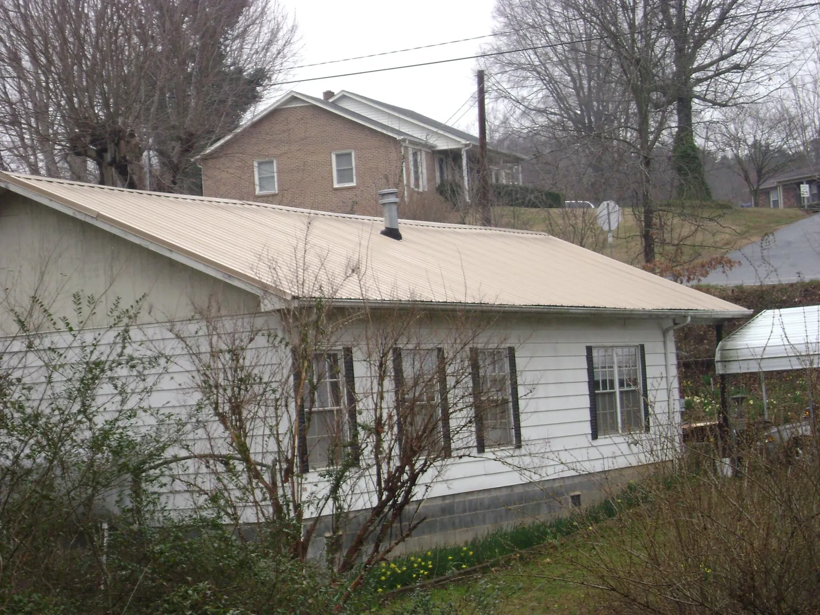 Tan metal roof on a white sided house set into a hillside — Commercial Roofing by Roofing Brothers in Anderson Island